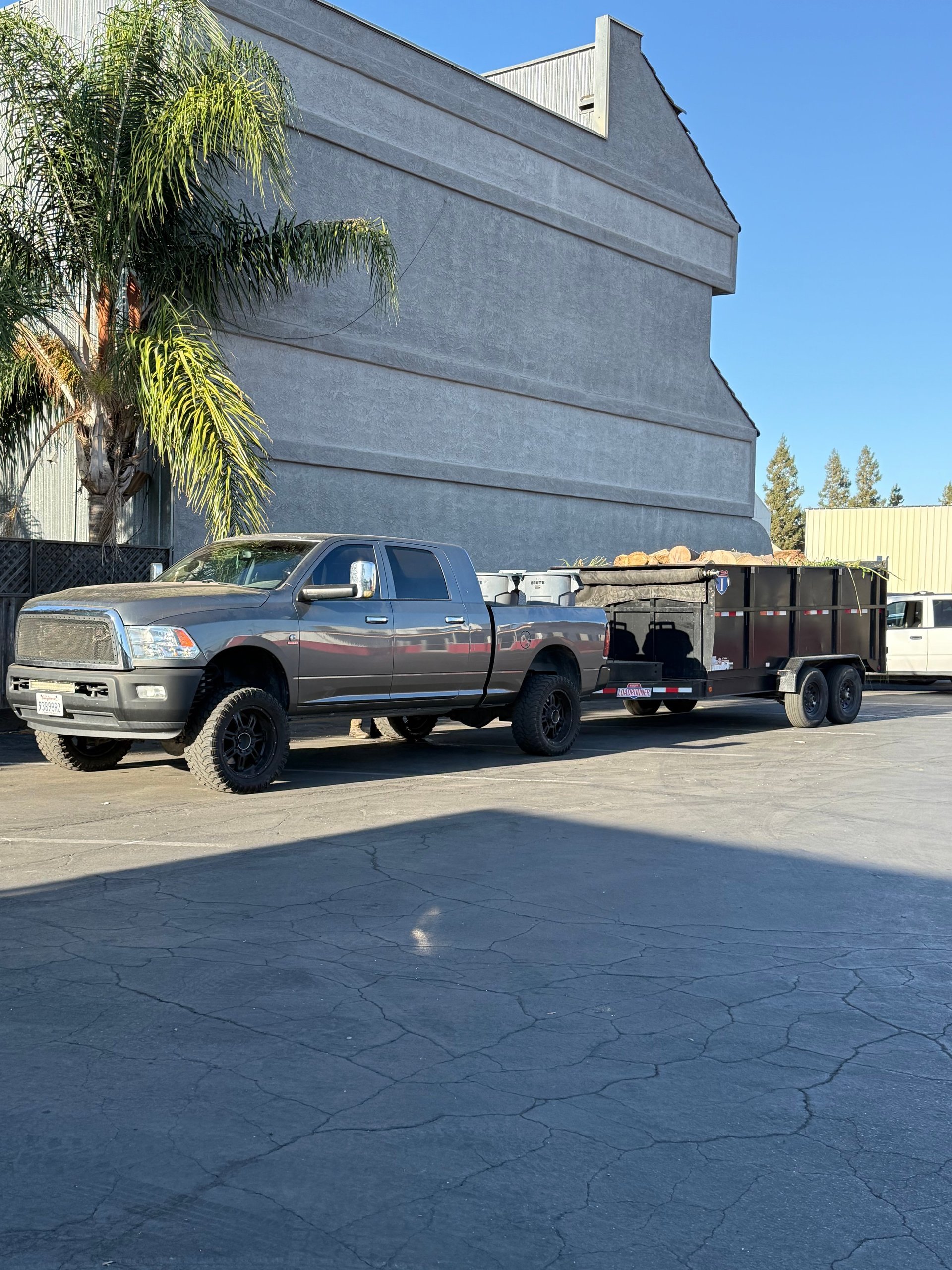 Silver pickup truck with attached flatbed trailer parked in front of large warehouse building